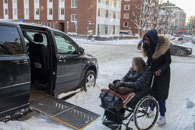 Carer helping woman on wheelchair to get into car