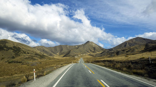 Empty road amidst mountains against sky at lindis pass, new zealand