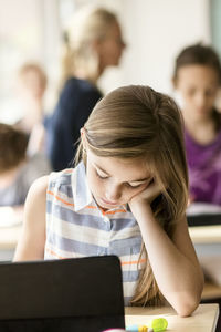 Schoolgirl studying with digital tablet at desk in classroom