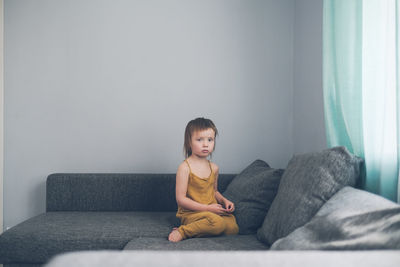 Cute sad european child sits alone on couch in real living room