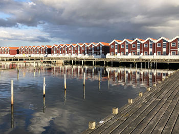 Pier on lake by houses against sky
