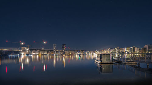 Boats moored in illuminated city against sky at night