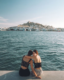 Rear view of female friends sitting on promenade against sky