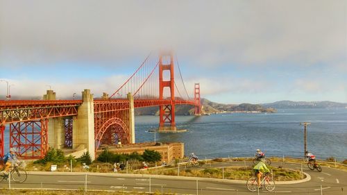 Cyclist riding bicycle on road below golden gate bridge over bay against sky