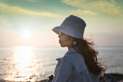 Mid section of woman wearing hat against sea during sunset