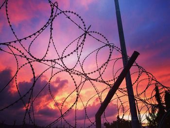 Low angle view of silhouette barbed wire against sky at sunset