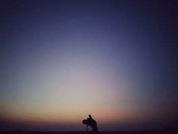 Cropped image of hand holding camera against sky at dusk