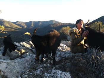 Mature woman herding mountain goats against sky