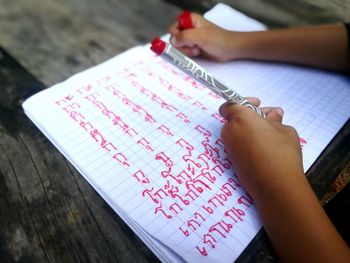 Cropped hand of child writing in book on table