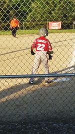 Rear view of man playing with chainlink fence