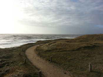 High angle view of footpath leading towards sea against cloudy sky