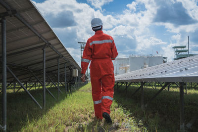 Rear view of worker wearing reflective clothing while standing on solar panel against sky