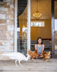 Woman sitting in the doorway of house and feeding the domestic birds