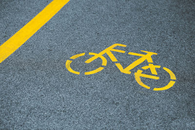 Yellow bicycle sign on cycling path, safe road traffic near highway. painted bicycle road sign