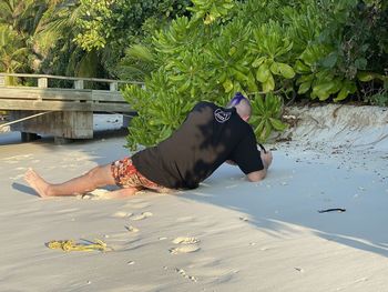 Man lying down on beach against trees