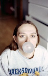 Portrait of young woman blowing bubble gum at home