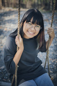 Portrait of smiling woman sitting on swing at playground