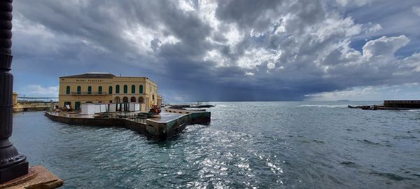 Buildings in sea against cloudy sky