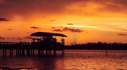 Silhouette built structure by sea against orange sky