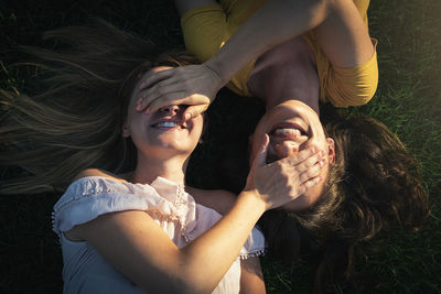 High angle view of lesbian couple covering eyes with hands while lying on land