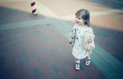 High angle view of cheerful girl holding stuffed toys on footpath