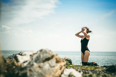 Woman kneeling at beach against sky