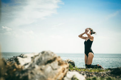 Young woman standing on rock by sea against sky