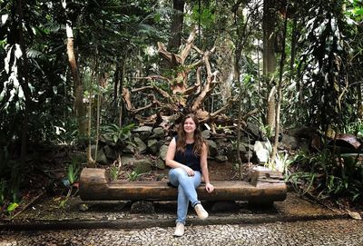 Portrait of smiling young woman sitting on tree trunk