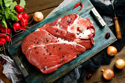 Fresh beef veal meat on rustic wooden table with fresh vegetables, top view