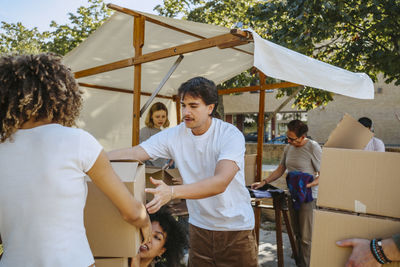 Male volunteer helping female colleagues while holding cardboard boxes during charity drive at community center