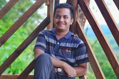 Portrait of smiling young man sitting against railing