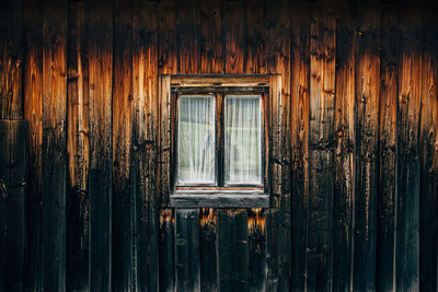 Old window with white curtain in wooden wall