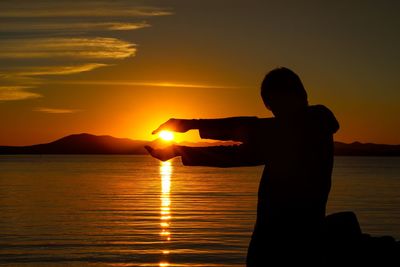 Silhouette man standing by sea against sky during sunset