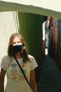 Beautiful young woman wearing coronavirus mask standing against wall