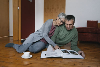 Senior couple sitting on the floor at home looking at photo album