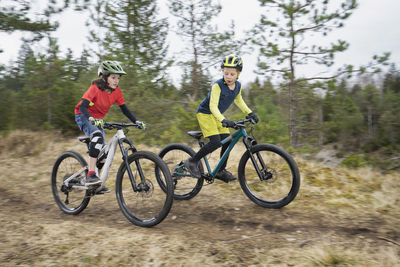 Brothers riding bicycle on dirt road in forest