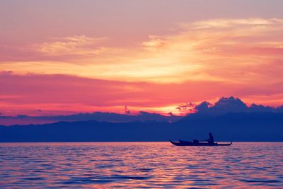 Silhouette man sailing boat in sea against orange sky