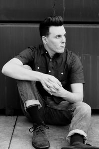 Young man looking away while sitting on footpath