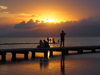 Silhouette people standing by sea against sky during sunset