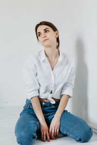 Portrait of young woman sitting against wall