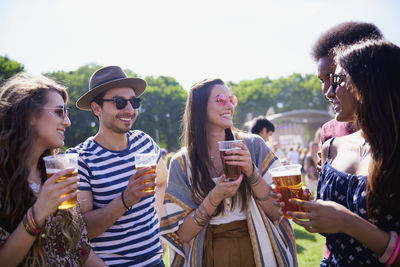 Friends holding drinks in glasses while standing against sky