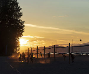 Silhouette people playing beach volleyball against sky during sunset