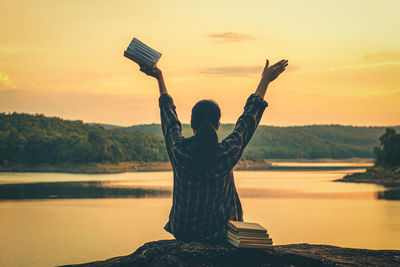 Woman standing by lake against sky during sunset