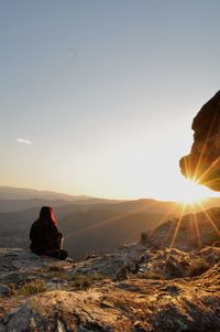 Rear view of woman sitting against mountains during sunset