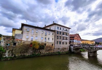 Bridge over river by buildings in city against sky