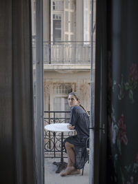 Side view of young woman sitting in window