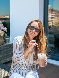 Smiling woman with sunglasses having a milkshake in rooftop