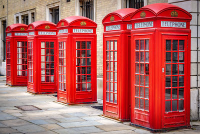 Red telephone booth on sidewalk by building in city