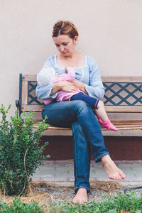 Mother breast feeding daughter while sitting on bench in yard