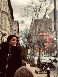 Young woman sitting on street amidst buildings in city